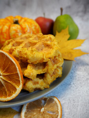on a gray background is a plate with three pumpkin gluten-free Belgian waffles next to a small pumpkin pear and apple and dried oranges.  side view.  breakfast .  diet