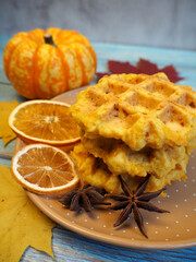 on a blue table with a yellow maple leaf is a brown plate with three pumpkin gluten-free Belgian waffles next to a small pumpkin, star anise and dried oranges.  breakfast .  diet autumn