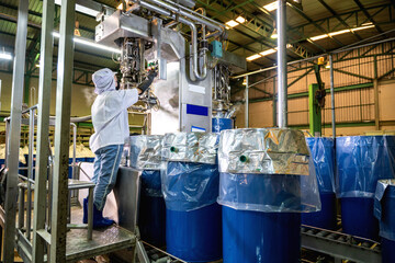 A worker controls an automatic aseptic filling machine filling ketchup into large drums at an...