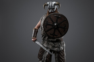 Studio shot of antique northern warrior with shield and sword against grey background.