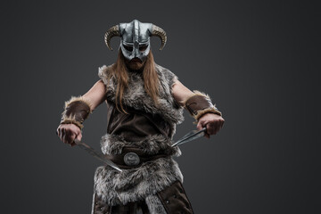 Shot of long haired viking from past with fur and helmet holding two daggers.
