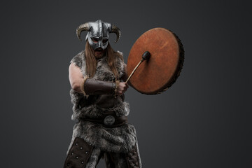 Portrait of barbaric warrior from north with drum dressed in fur and helmet.