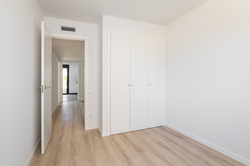 Empty white room without furniture, with built-in wardrobe with wooden laminate flooring, ventilation and access to the corridor. Concept of a studio or apartment for rent. Copyspace