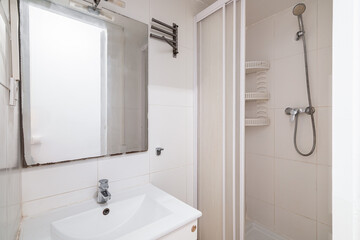 Compact white old tiled bathroom with shower and sink in need of renovation. Concept of preparing the premises for the redesign and dismantling of tiles and plumbing