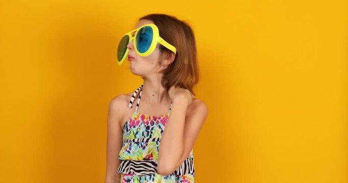 Child teenager girl in swimsuit and big sunglasses posing, having fun, make faces in studio on yellow background, summer mood,