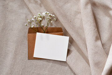Empty paper card with mockup copy space, envelope with flowers on neutral beige linen background,...