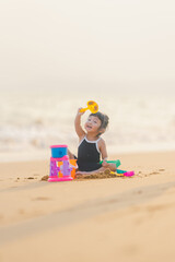 happy time of cute girl in dress black sit play sand scoop toy set on the beach with blur background beautiful sunset in the sea
