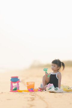 happy time of cute girl in dress black sit play sand scoop toy set on the beach with blur background beautiful sunset in the sea