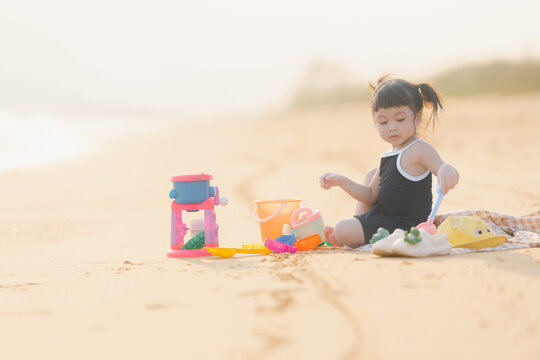 happy time of cute girl in dress black sit play sand scoop toy set on the beach with blur background beautiful sunset in the sea