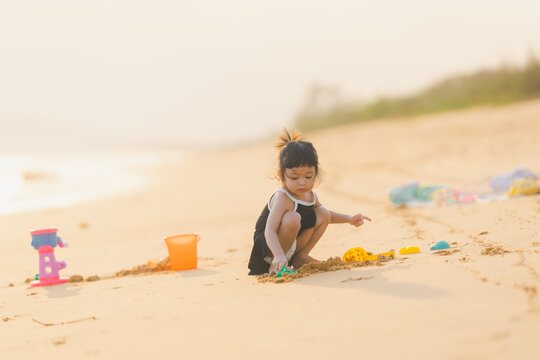 happy time of cute girl in dress black sit play sand scoop toy set on the beach with blur background beautiful sunset in the sea