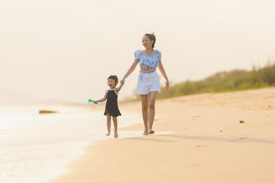 happy time of mom and daughter in dress black walking and run play on the beach with blur background beautiful sunset light in the sea