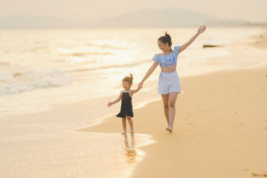 happy time of mom and daughter in dress black walking and run play on the beach with blur background beautiful sunset light in the sea
