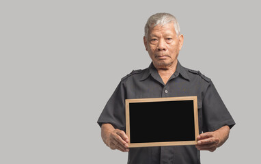 An elderly Asian man holding a mini blackboard and looking at the camera with a smile while standing on a gray background