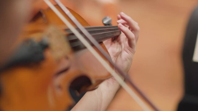 A slow motion video of a musician playing the violin with a bow during a classical symphony orchestra rehearsal