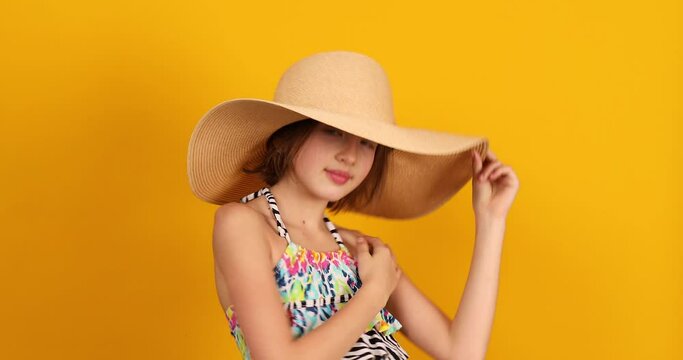 Child teenager girl in swimsuit and straw hat posing in studio on yellow background, summer mood,