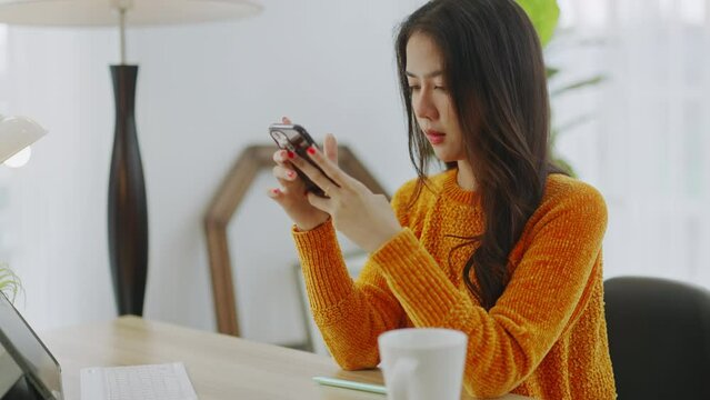 Young asian woman relax on comfortable couch at home,smiling girl use cellphone,shopping online.asian female reading good news on phone,browse wireless internet on gadget,chatting in living room