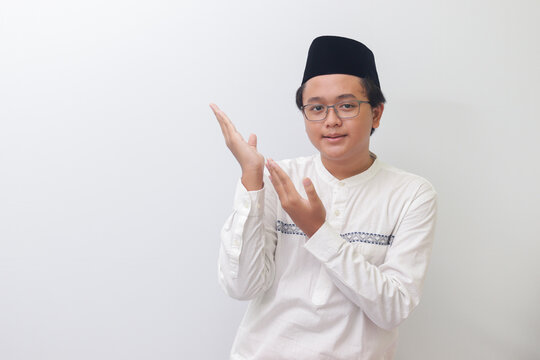 Portrait of young Asian muslim man showing product and pointing with his hand and finger. Isolated image on white background
