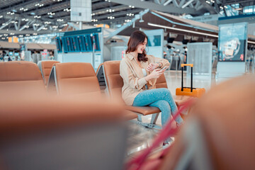 Happy attractive asian woman looking at her wrist watch while waiting in airport terminal, copy...