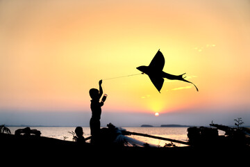 Fototapeta na wymiar Silhouette of rural children flying kites at sunset.