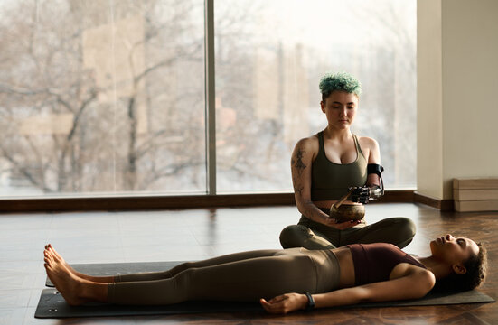Young woman lying on the floor and relaxing while yoga instructor using singing bowl