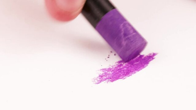 Drawing with a purple crayon on a piece of paper.