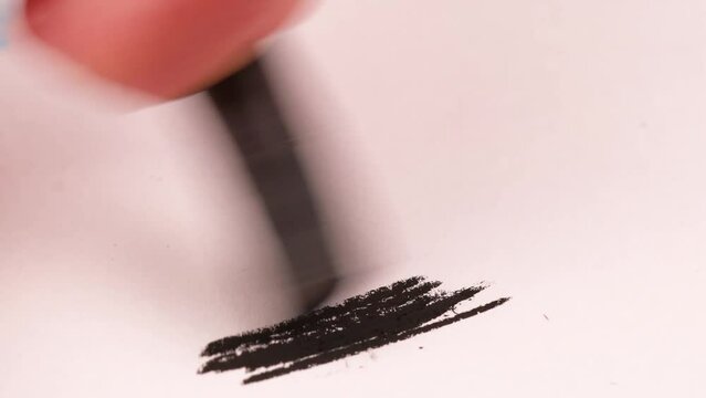 Drawing with a black crayon on a piece of paper.