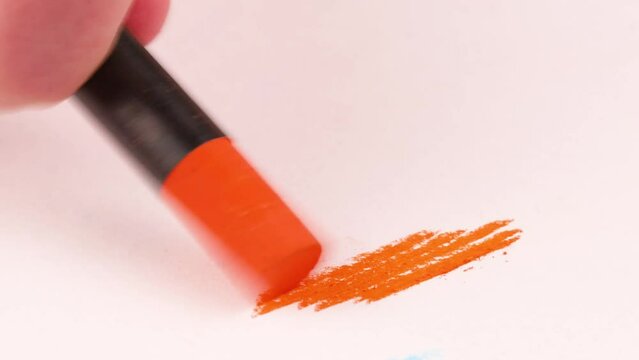 Drawing with an orange crayon on a piece of paper.