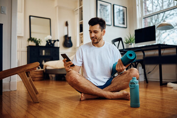Happy athlete texting on cell phone while exercising at home.