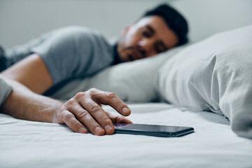 Close up of man turning off alarm on his phone in morning in bed.