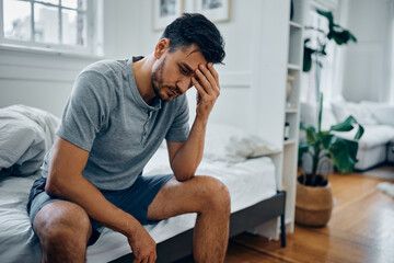 Distraught man thinks of something while sitting in bedroom.