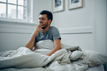 Fototapeta premium Tired man yawning while waking up at home.