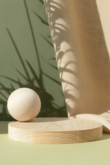 Wooden cylindrical podium, pedestal on a green background with beige curtain and a shadow of palm...