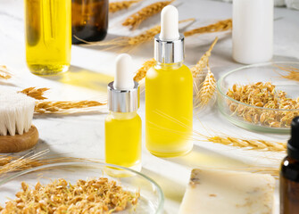 Wheat serum oil for skin and hair care. A conceptual composition of wheat essential oils, a bath brush and wheat germ on a marble table. Bottle of body oil with a dropper. Self-care, spa and wellness