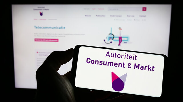 Stuttgart, Germany - 03-12-2023: Person holding cellphone with logo of Dutch regulator Autoriteit Consument en Markt (ACM) on screen in front of webpage. Focus on phone display.