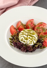 Burrata cheese with tomatoes and fresh greens on a white porcelain plate