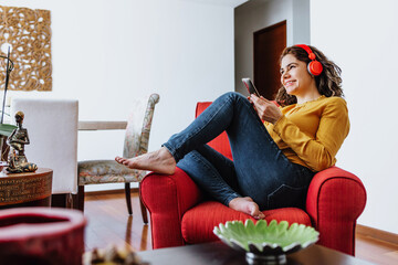 latin adult woman using phone and headphones resting on sofa at home in Mexico, Hispanic female lifestyles