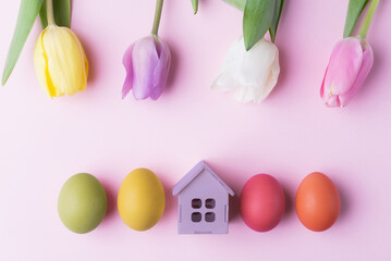Easter eggs, tulip flowers and decorative house on pink background with copy space. Easter holiday greeting concept