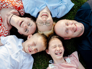Close-up Top view of a laughing happy family with three children lying on a grassy lawn with their heads to each other