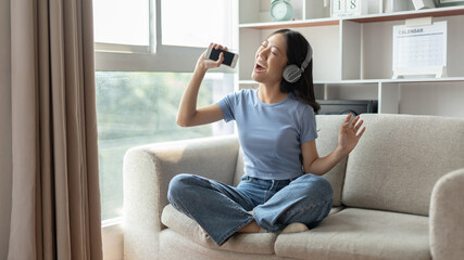 Obraz premium Young Asian woman happily listening to music through headphones, Woman was enjoying listening to her favorite music and rocking to the beat of the music, Stress relief, Happiness in life.