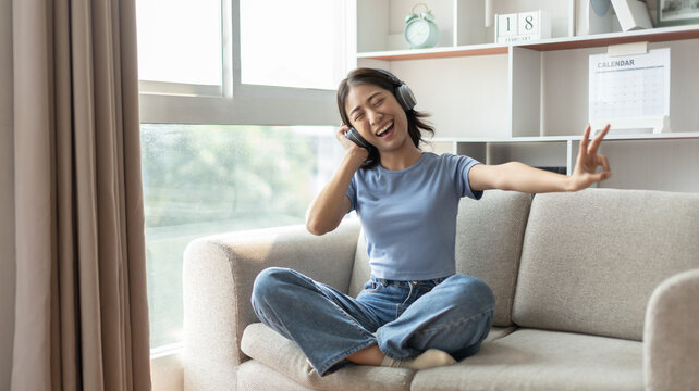 Young Asian woman happily listening to music through headphones, Woman was enjoying listening to her favorite music and rocking to the beat of the music, Stress relief, Happiness in life.