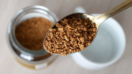 Close-up of a beautiful spoon filled with freeze-dried instant coffee above the coffee jar and an empty cup on the table
