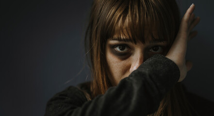 Portrait picture of beaten woman standing in front of a dark wall - Stop violence against women...