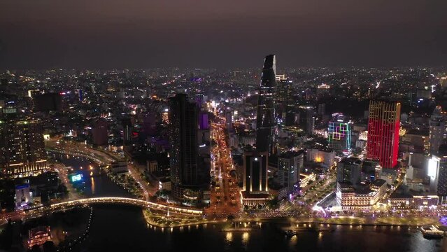 Ho Chi Minh City, Vietnam iconic Skyline and Saigon river waterfront aerial panorama on a busy night featuring all key buildings illuminated with colored lights. Aerial crane shot.