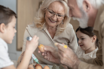 Grandma smiling while her grandkids decorate Easter eggs