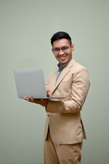 Successful Asian businessman holding his laptop, standing against green studio background.