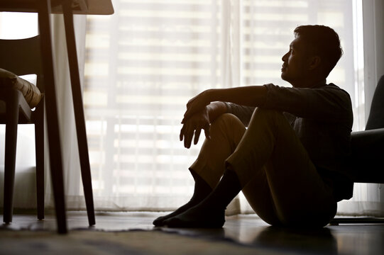 Depressed and frustrated Asian man sits on the living room floor, dark room - Powered by Adobe