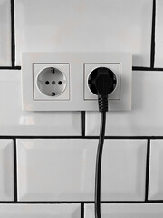 The electrical outlet on the wall, white black plug socket 