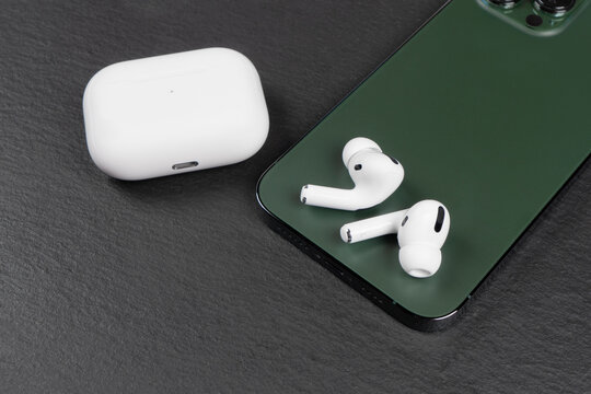 Modern wireless earbuds headphones with charging case and smartphone on stone table background. Earphones for smartphone and tablet