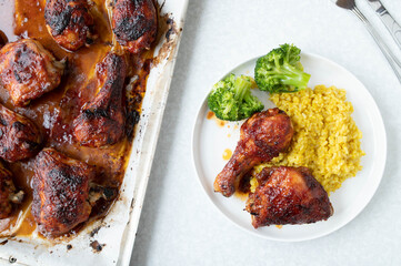 Glazed chicken on a baking sheet served  with curry brown rice and broccoli on a plate. Flat lay