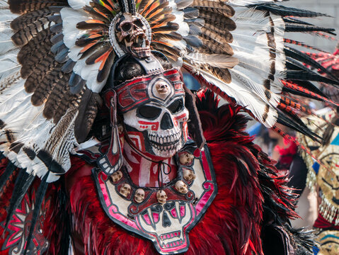 Traje ceremonial azteca presenta una m&aacute;scara de calavera y un tocado de plumas vibrantes durante una celebraci&oacute;n cultural de herencia prehispanica. D&iacute;a de los Muertos en el Z&oacute;calo de M&eacute;xico